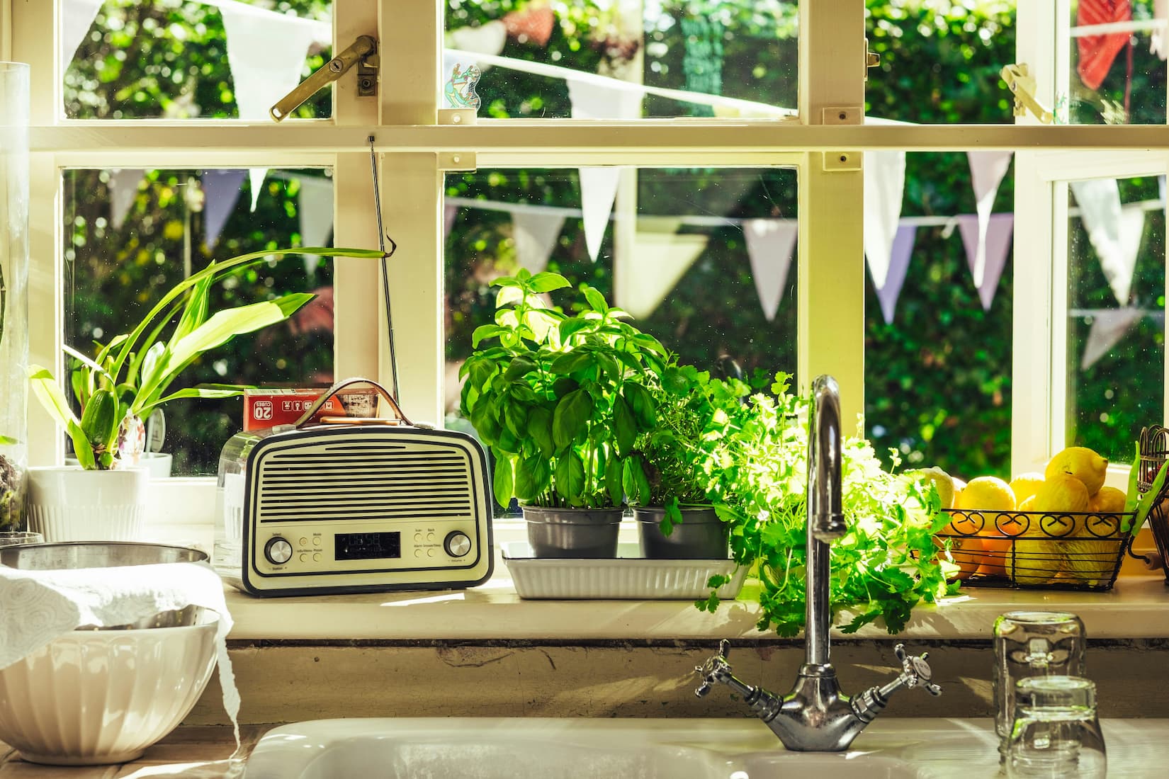 Sun-filled kitchen windowsill with fresh herb plants, lemons, and garden greenery — botanical fragrances and green fragrance notes that show how to make your home smell good in summer